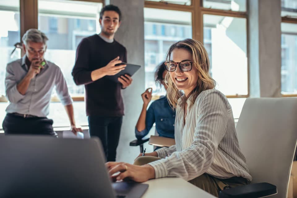 Smiling professional working on a laptop with colleagues collaborating in a bright modern office